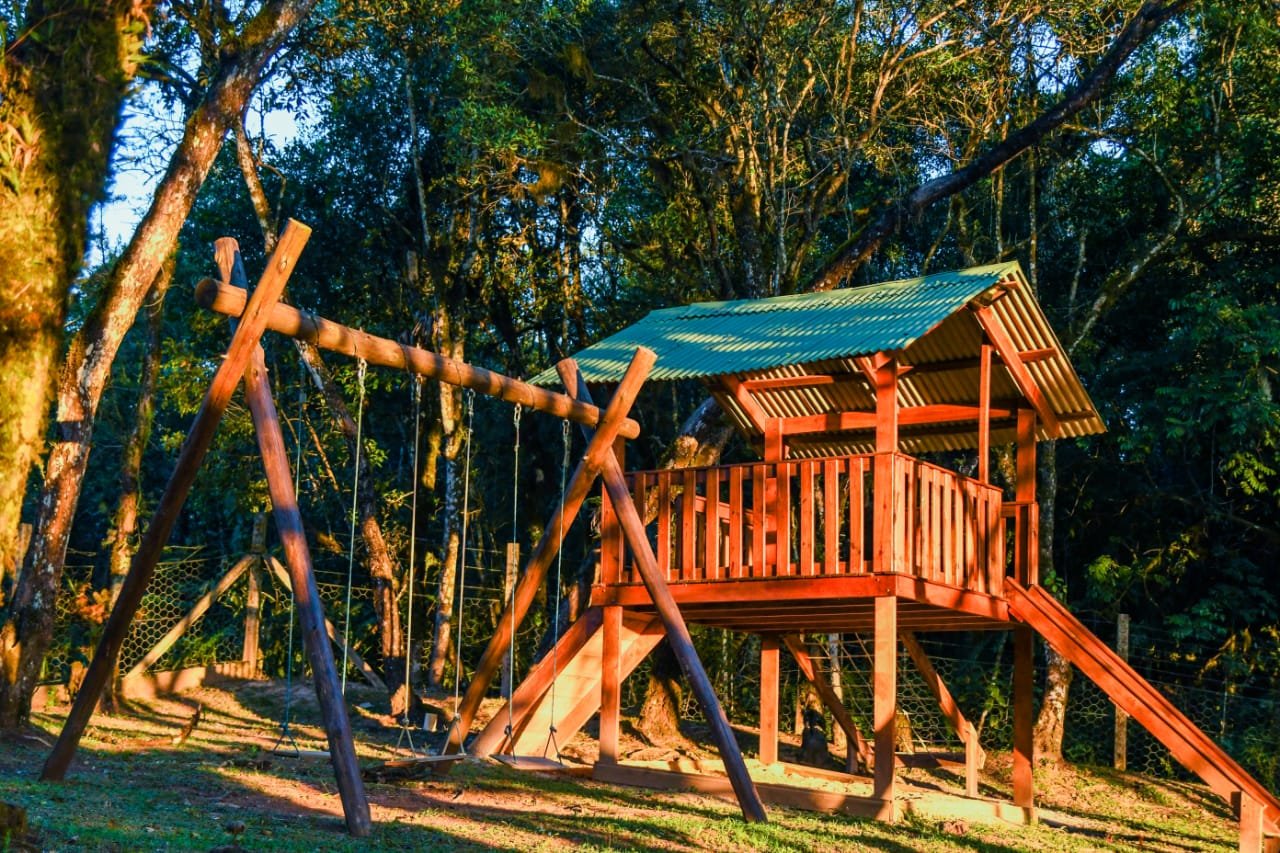 Espaço kids com casa na árvore e balanços